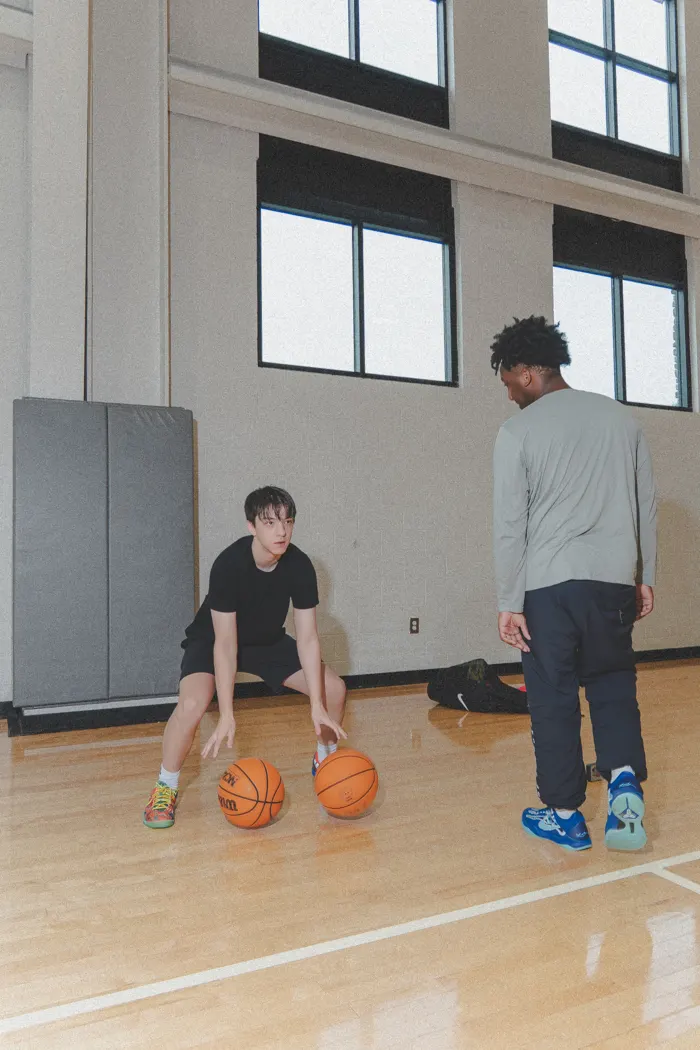 A Sevenity trainer coaching an athlete through a two-ball dribbling drill in the gym